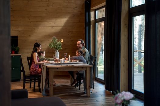 A family enjoying dinner in a cozy, modern wooden cabin with warm lighting.