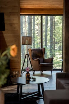 Elegant armchair and lamp in a cozy wooden cabin with forest view.