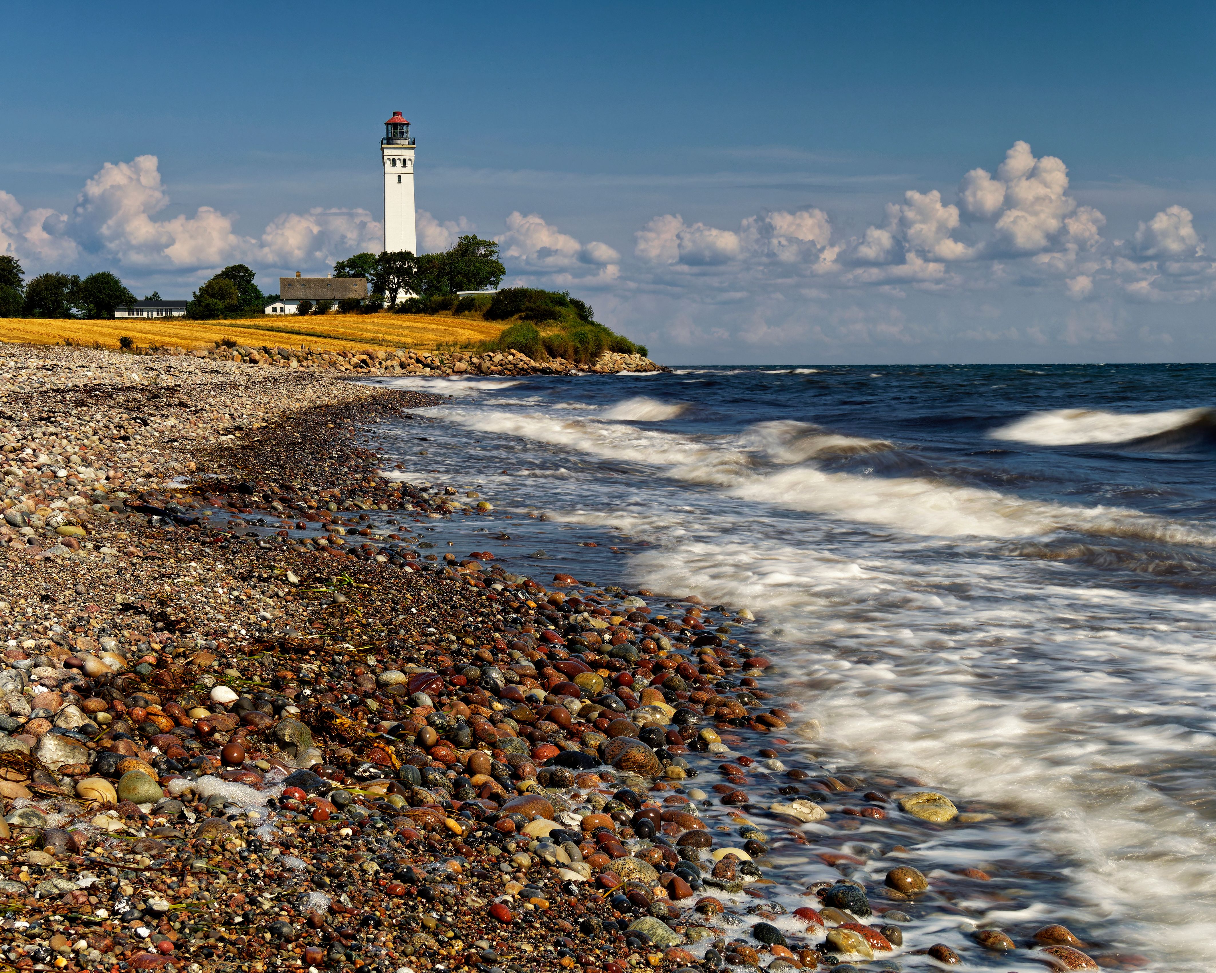 Scenic view of a lighthouse on a rocky beach with waves crashing in Denmark.