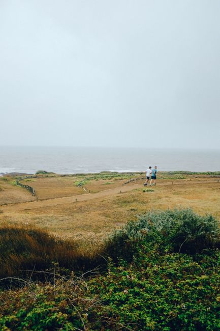 Two people run along a scenic coastline under a misty sky, capturing the essence of nature and outdoor activity.