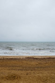 A serene beach scene with overcast skies and gentle waves on a sandy shore.