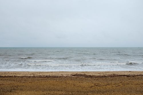 Free Peaceful beach scene with gentle waves under an overcast sky, perfect for relaxing moments. Stock Photo