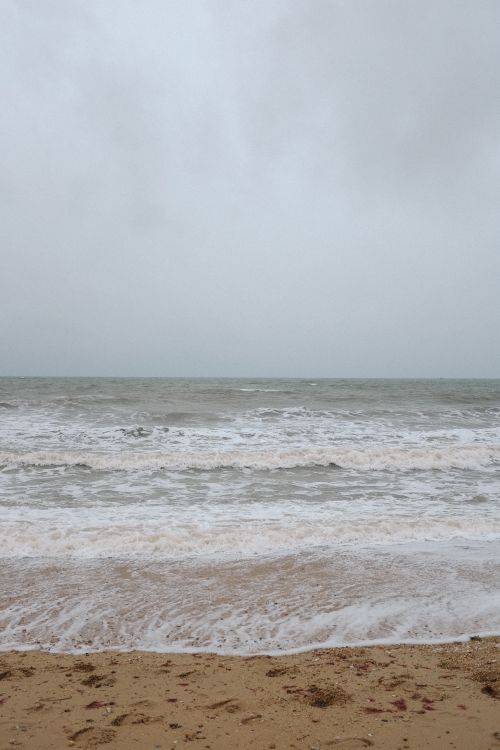 Free Peaceful ocean view with gentle waves crashing on a sandy shore under a cloudy sky. Stock Photo