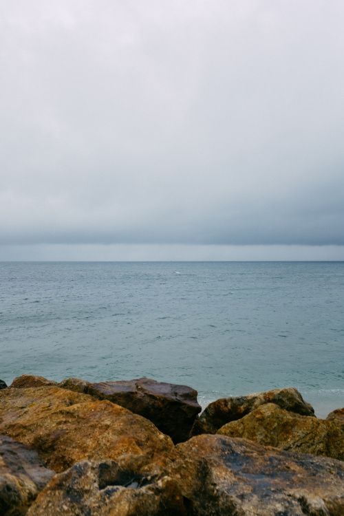 Free A peaceful ocean view with a rocky shoreline under a cloudy sky. Stock Photo