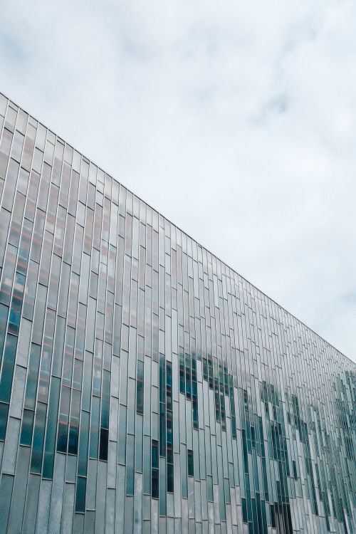Free Sleek architectural design featuring vertical glass panels under a cloudy sky. Stock Photo