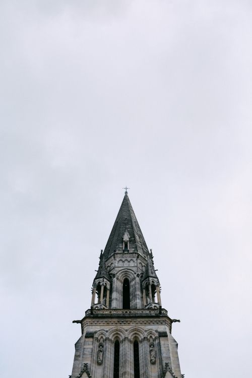 Free A stunning low-angle view of a Gothic church steeple reaching into a white sky. Stock Photo