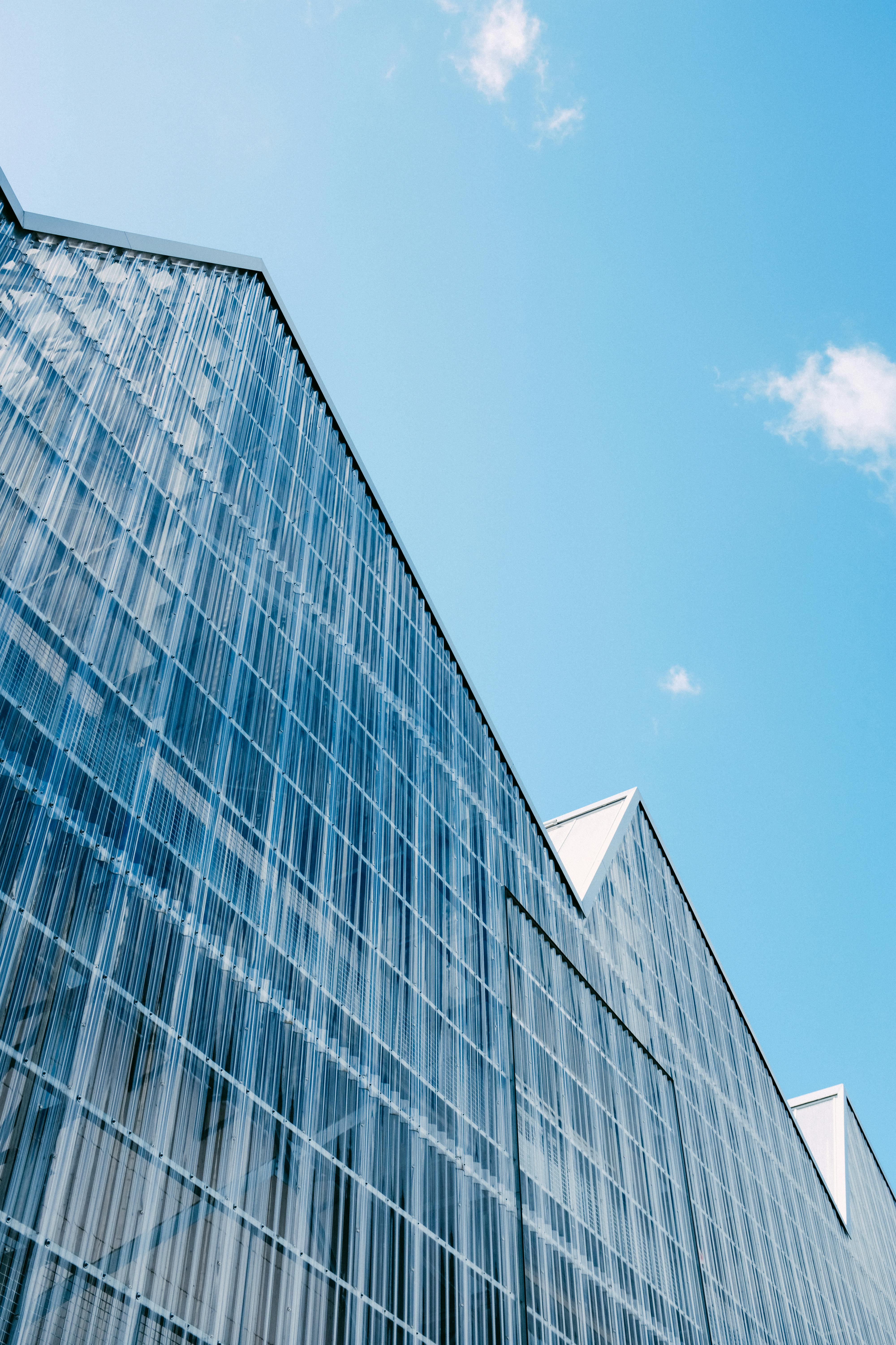 Low angle view of a modern building with a glass facade and blue sky in the background.