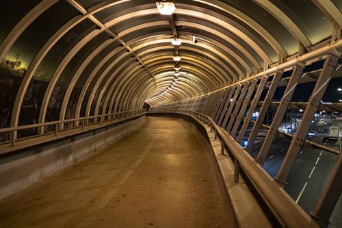 Free A well-lit urban walkway tunnel arching over a busy road at night. Stock Photo