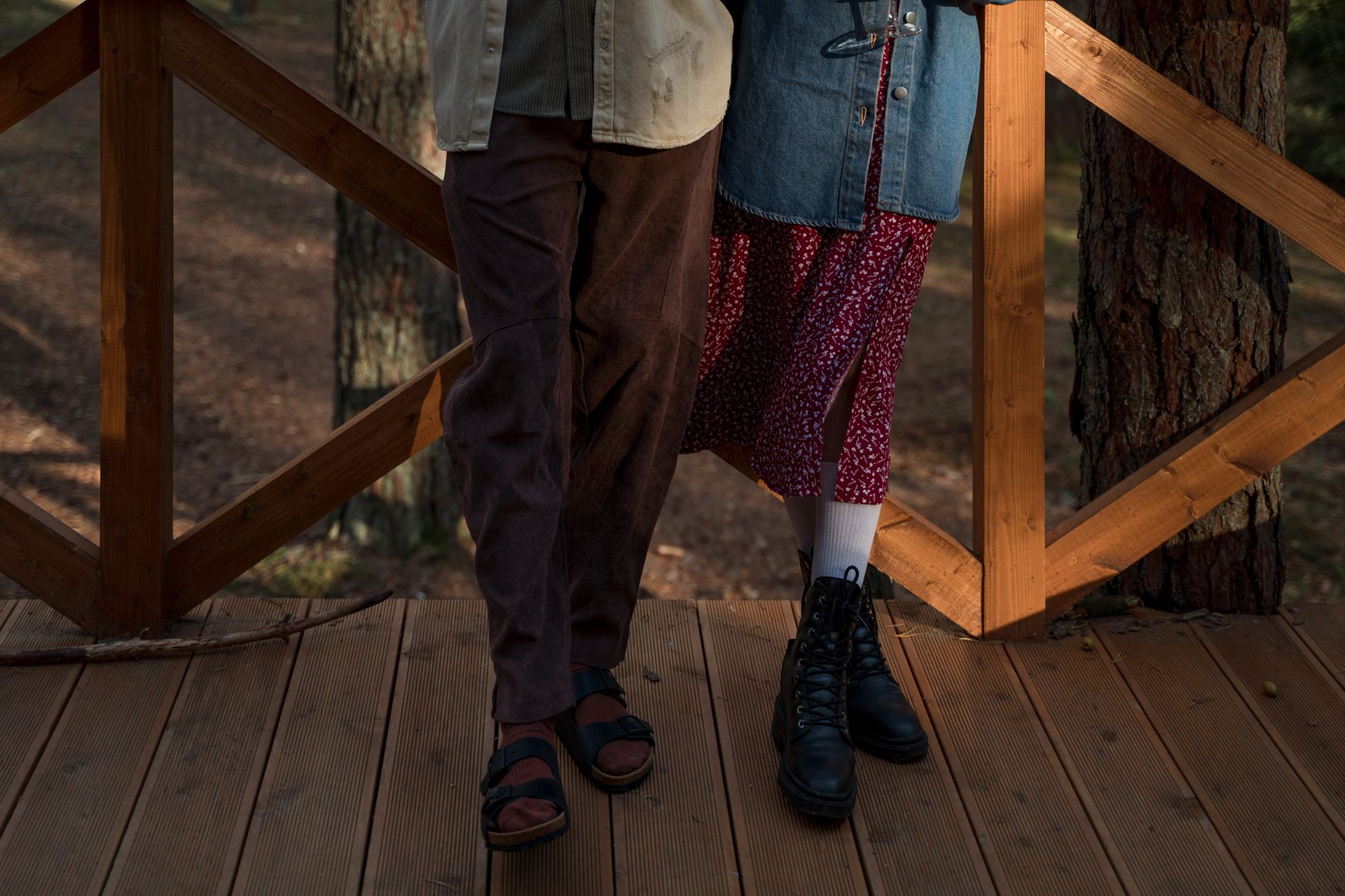 Legs of a couple standing on a rustic wooden deck amidst a serene forest setting.