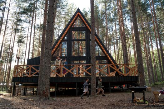 A happy family gathers at a modern wooden cabin in a peaceful forest setting.