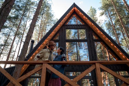 Free Man and woman share a romantic moment with wine at a forest cabin. Warm and cozy atmosphere. Stock Photo