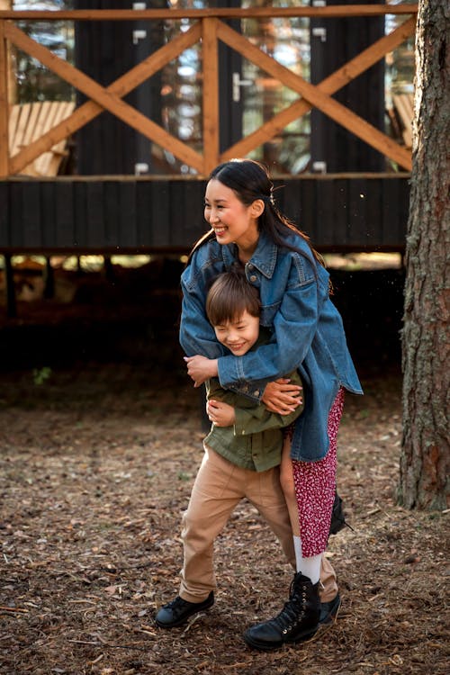 Woman in Blue Jacket and Green Pants Standing Near Brown Wooden Bridge