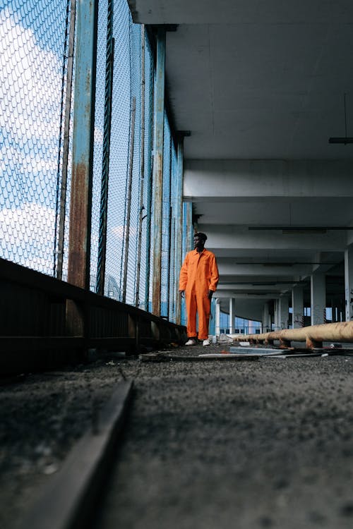 Man in Orange Overalls Standing Beside a Fence