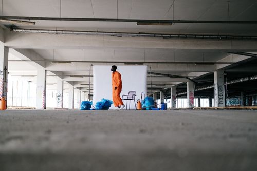 Free A man in orange overalls stands with trash bags in an urban parking garage. Stock Photo