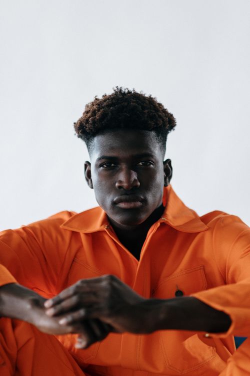 Free Close-up portrait of a man posing in a bright orange outfit with a neutral background. Stock Photo