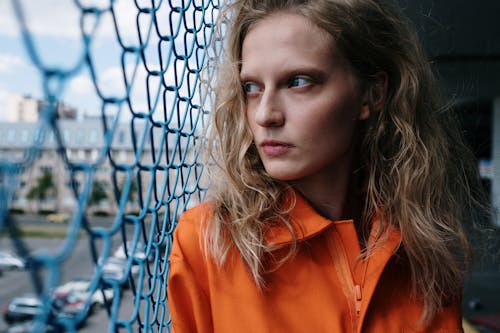 A Woman in Orange Polo Leaning on Chain Link Fence