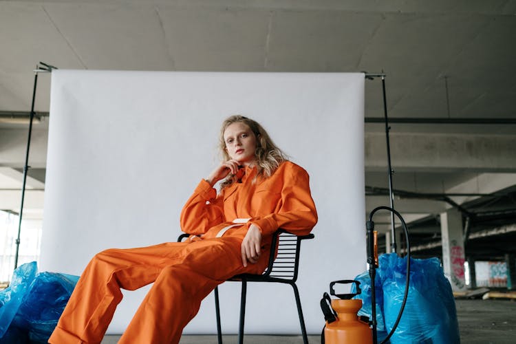 A Low Angle Shot Of A Woman In Orange Jumpsuit Sitting On A Chair