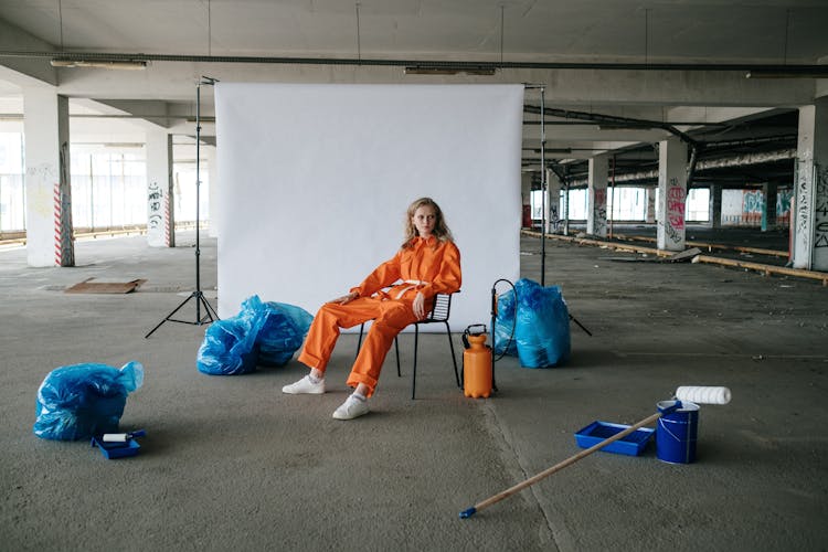 A Woman In Orange Jumpsuit Sitting On The Chair