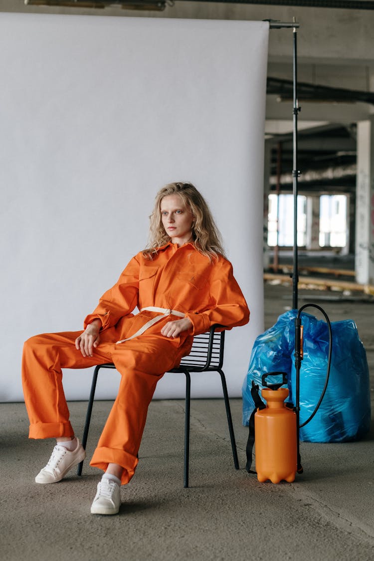 A Woman In Orange Jumpsuit Sitting On A Chair