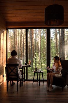 A man and woman working from home in a scenic cabin surrounded by forest.