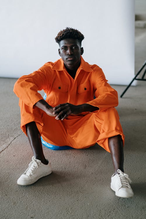 A Man in Orange Overalls Sitting on Gray Concrete Floor