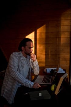 A man is deeply concentrating on his laptop while seated at a desk, basked in warm sunlight.
