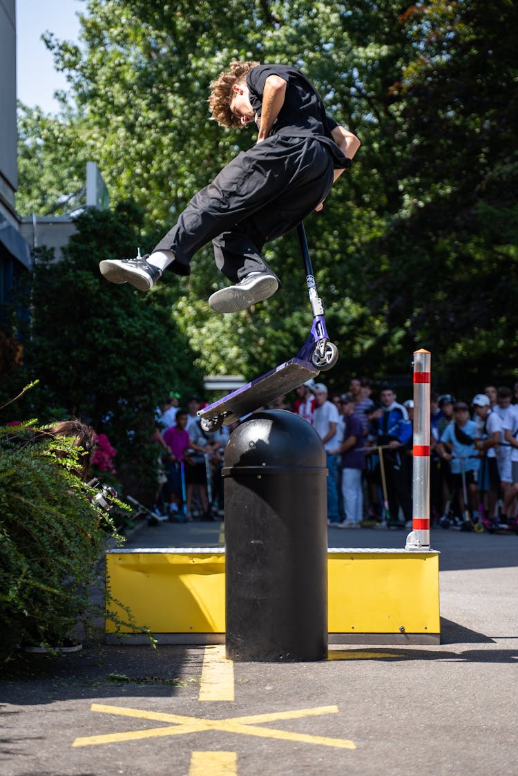 Man In Black Shirt And Black Pants Riding On A Kick Scooter Doing Tricks