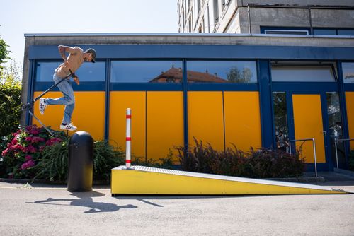 Free A man jumping a kick scooter over a ramp in an urban setting with a colorful backdrop. Stock Photo