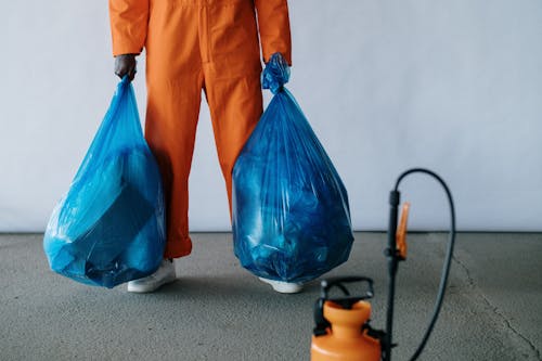 Man in Orange Overalls Holding Blue Bags