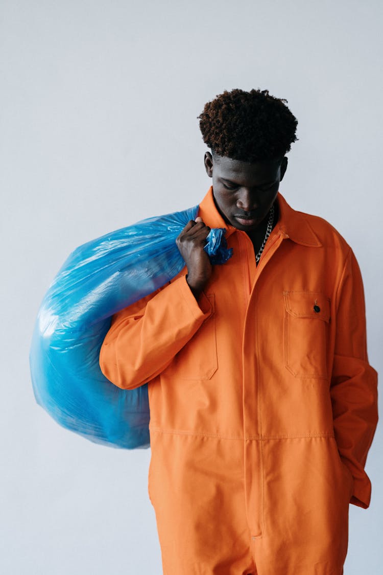 A Man In Orange Jumpsuit Carrying A Blue Plastic Bag