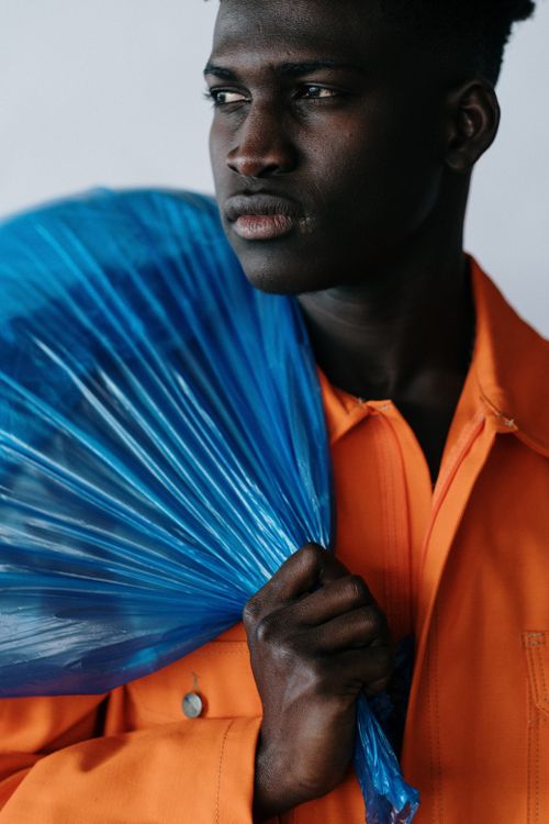 Free Portrait of a man in an orange jacket holding a blue plastic bag over his shoulder. Stock Photo