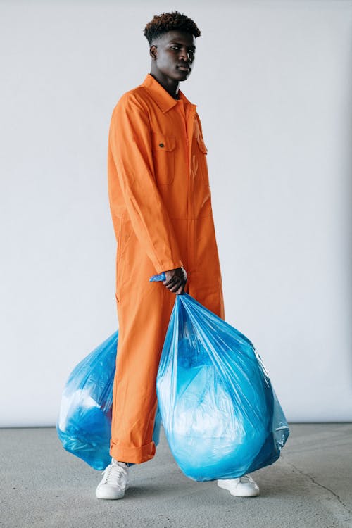Free A Man in Orange Jumpsuit Standing while Carrying Plastic Bags Stock Photo
