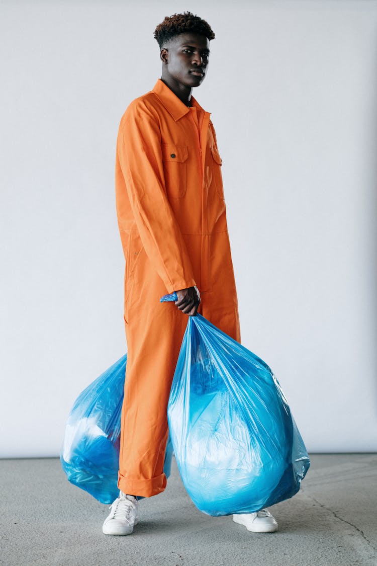 A Man In Orange Jumpsuit Standing While Carrying Plastic Bags