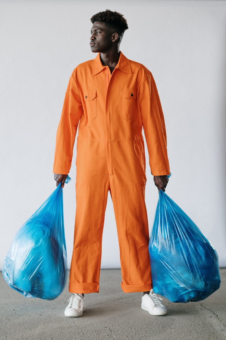 A Man In Orange Jumpsuit Standing While Carrying Plastic Bags