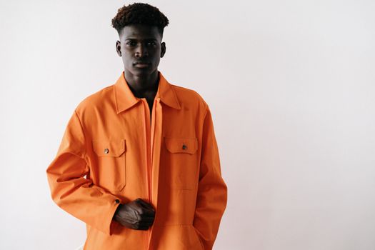 Portrait of a black man in stylish orange workwear posed against a white backdrop during a studio shoot.