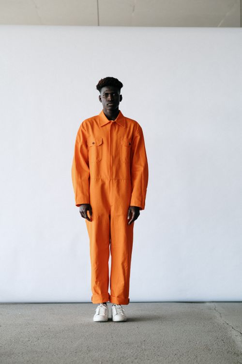 Free Full body shot of a man wearing an orange coverall, standing indoors. Stock Photo