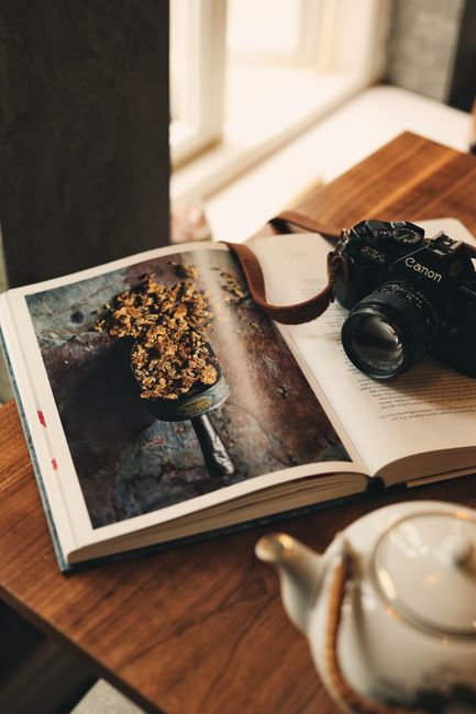 Warm-toned still life featuring an open book, camera, and teapot on a wooden table.