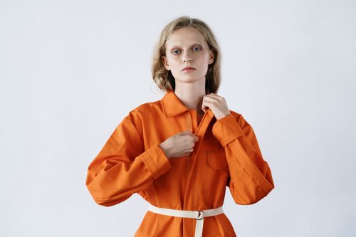 Free A woman poses confidently wearing a vibrant orange jumpsuit against a neutral background. Stock Photo