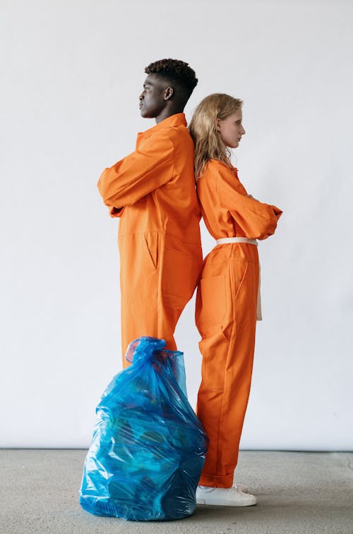 Man and Woman in In Orange Coveralls Standing Back To Back 