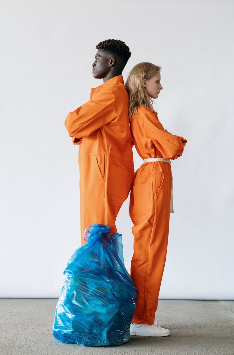 Man And Woman In In Orange Coveralls Standing Back To Back 