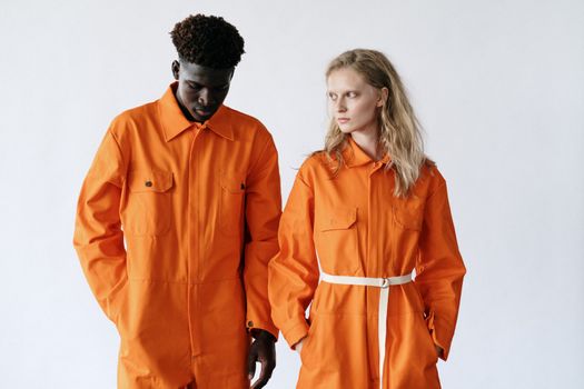 Two adults wearing bright orange work uniforms stand against a neutral white background.