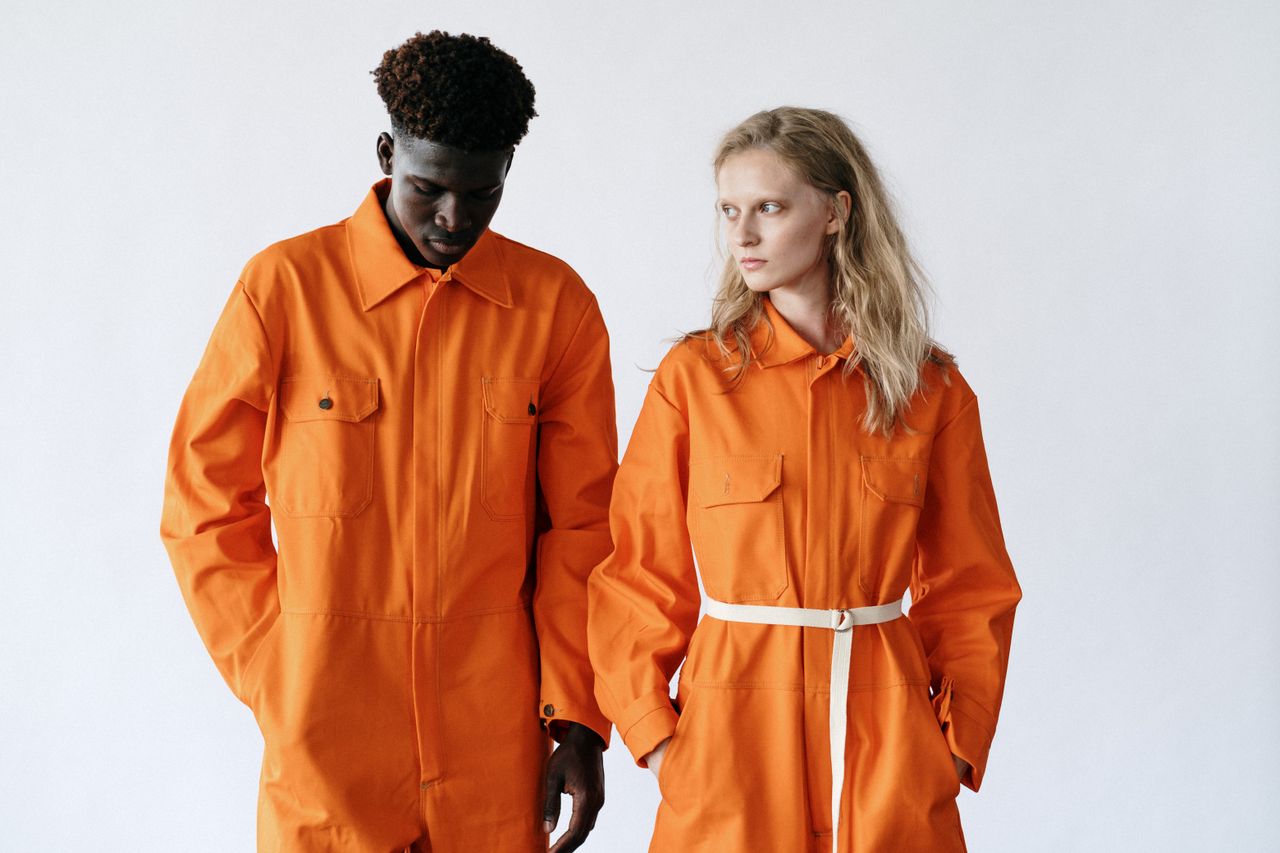 two adults wearing bright orange work uniforms stand against a neutral