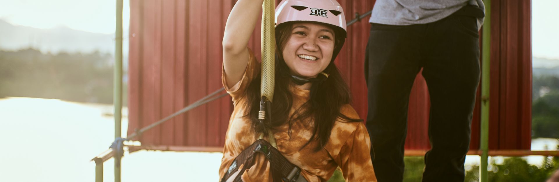 Girl excitedly zip lining outdoors with safety gear on a sunny day.