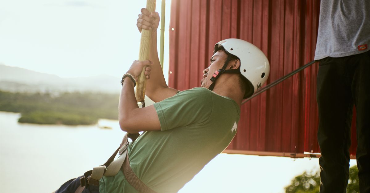 Man enjoying a thrilling zip line ride with a scenic background at sunset.
