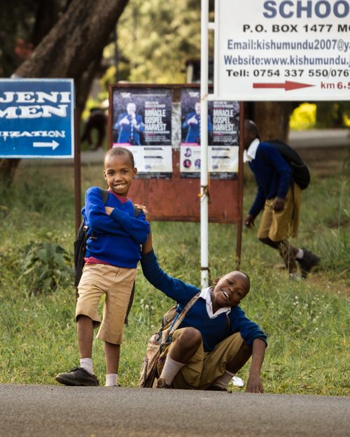 Free African boys in school uniforms smiling and playing outdoors near a school sign. Stock Photo