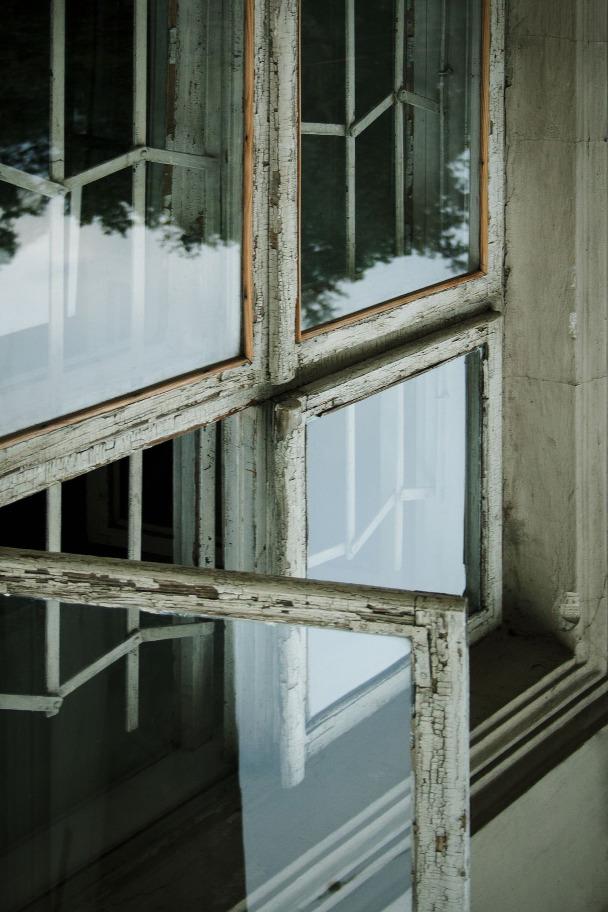 Nahaufnahme eines stark verwitterten Holzfensterrahmens mit abblätternder Farbe und sichtbaren Rissen an der Fuge