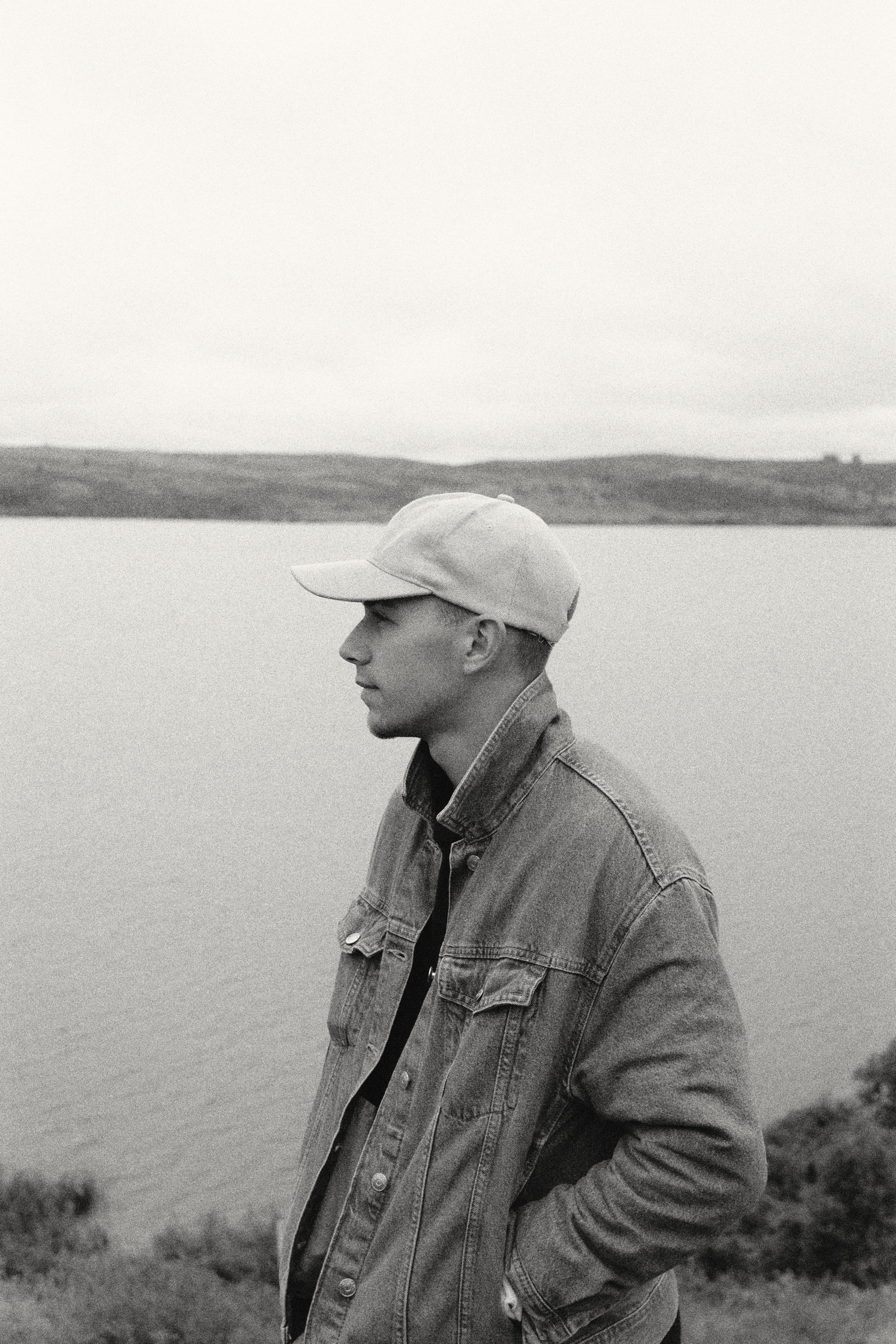 A man in casual denim attire gazes over a serene riverscape.