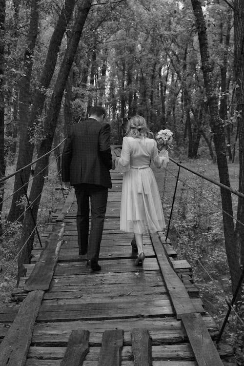Black and White Photo of a Bride and Groom Crossing on a Wooden Pathway