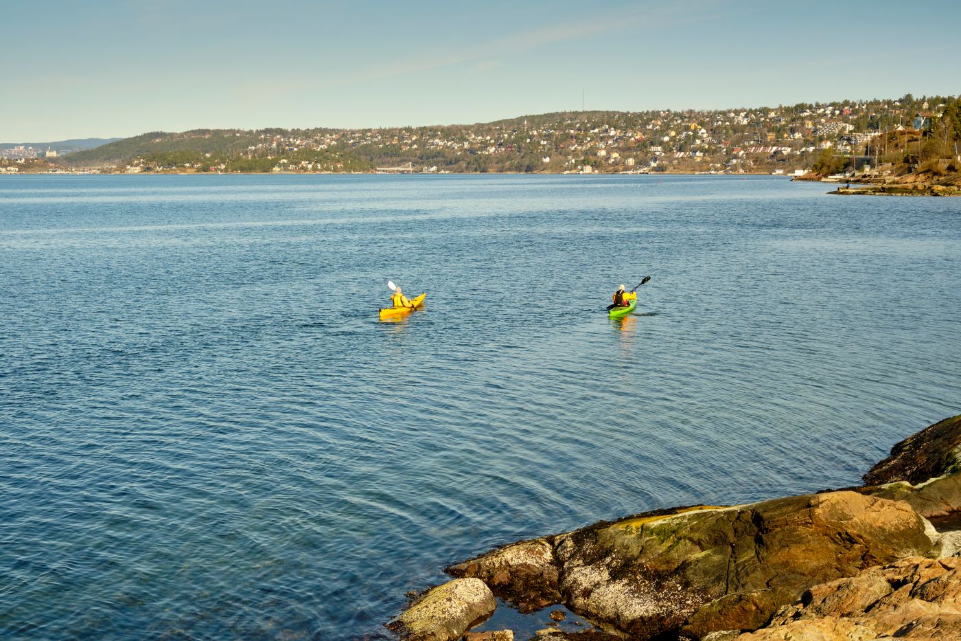 Two kayakers paddling on calm blue coastal water
