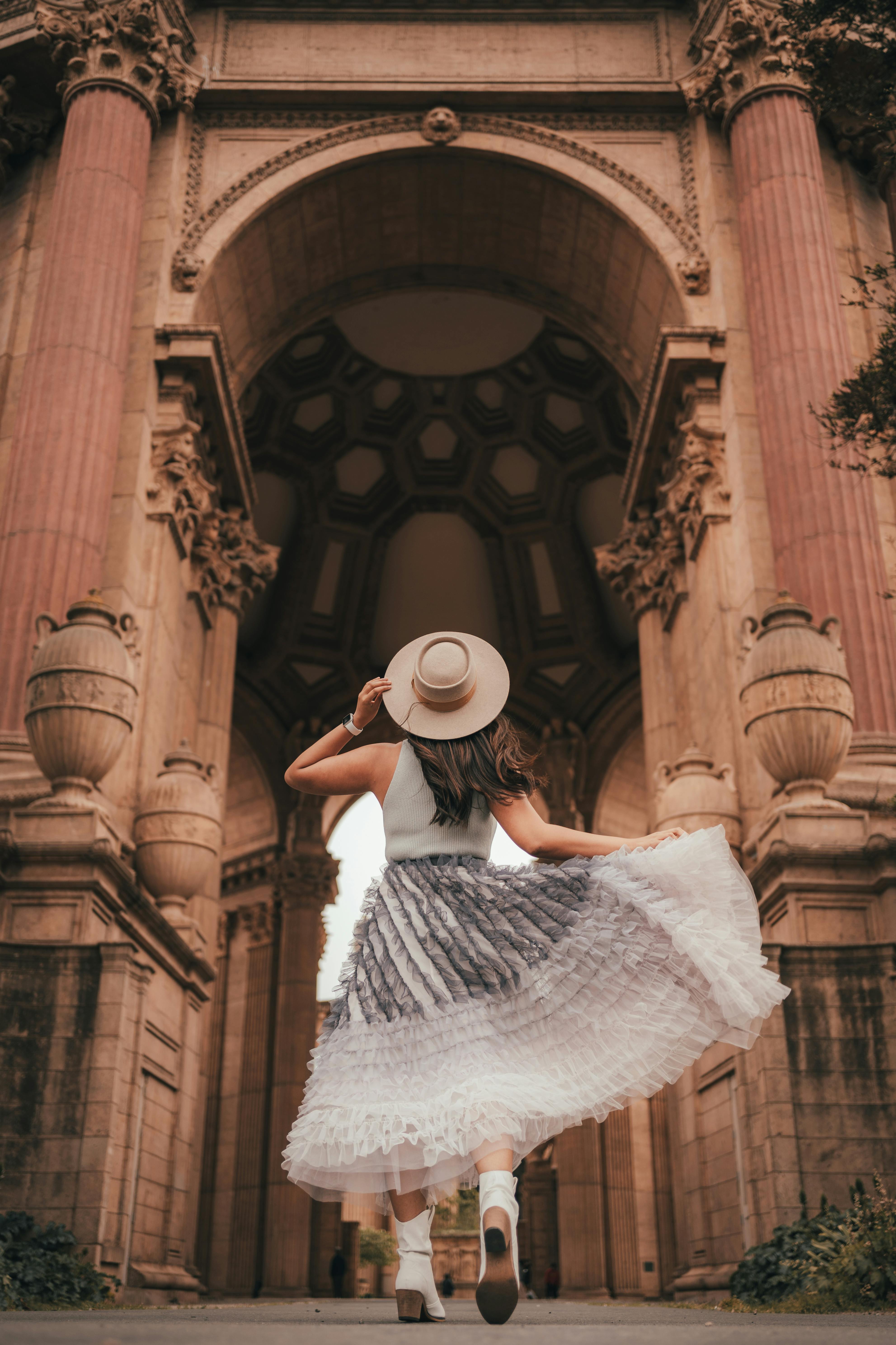 A stylish woman in a flowing dress poses at a grand historic archway, capturing elegance and architectural beauty.